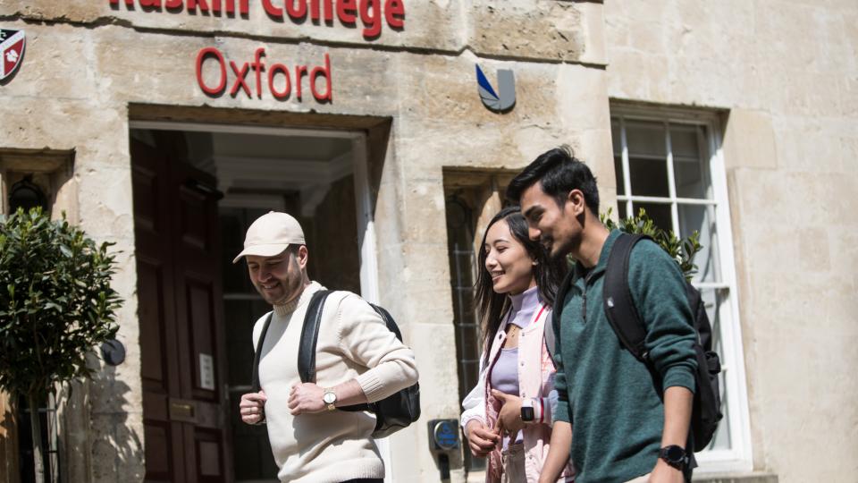 A close-up of three students walking across the entrance to Ruskin College Oxford on a sunny day.