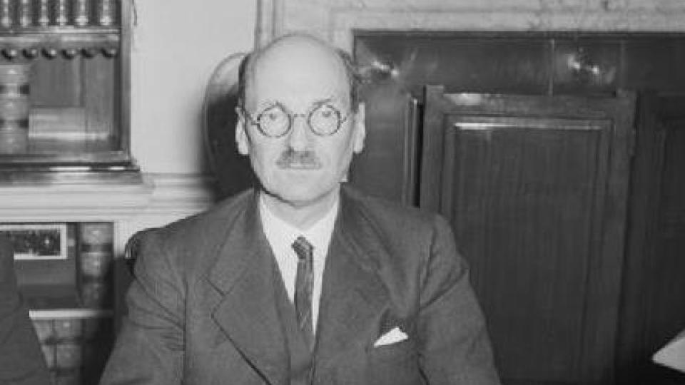 Clement Attlee is wearing a suit and tie and has glasses on.