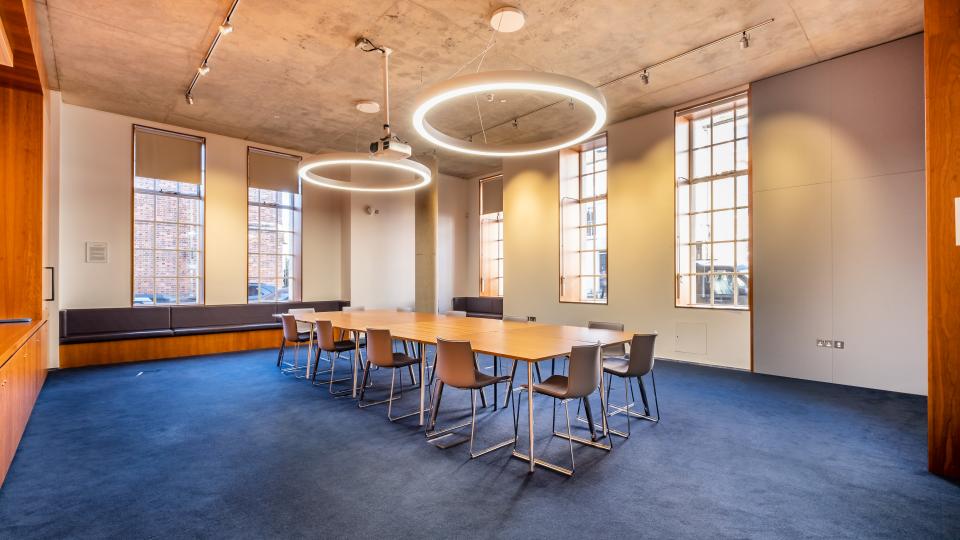 Exeter College Ruskin Room features two circular lights above a long table, and blue carpeting.