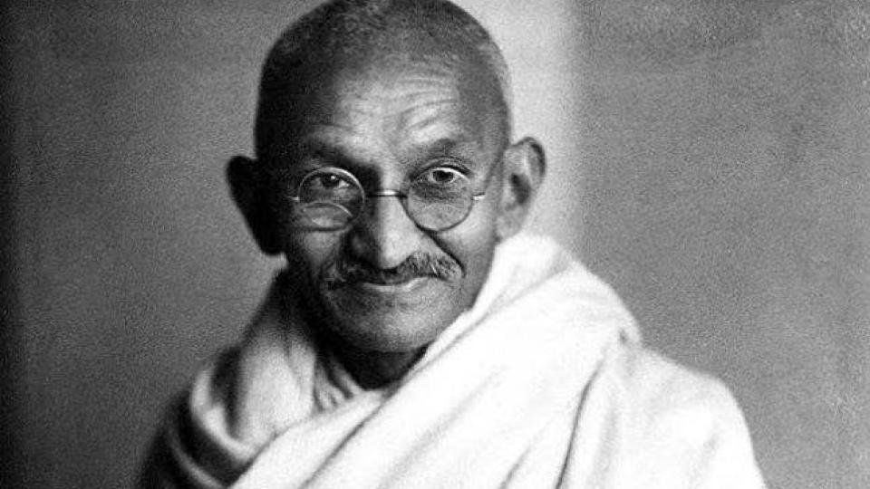 Mahatma Gandhi is wearing glasses in a light garment.