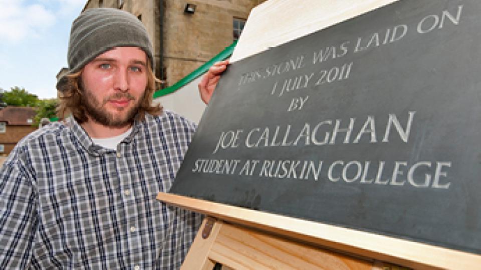 A man standing outside The Rookery, with a plaque stating "This stone was laid on 1 July 2011 by Joe Callaghan, student at Ruskin College"