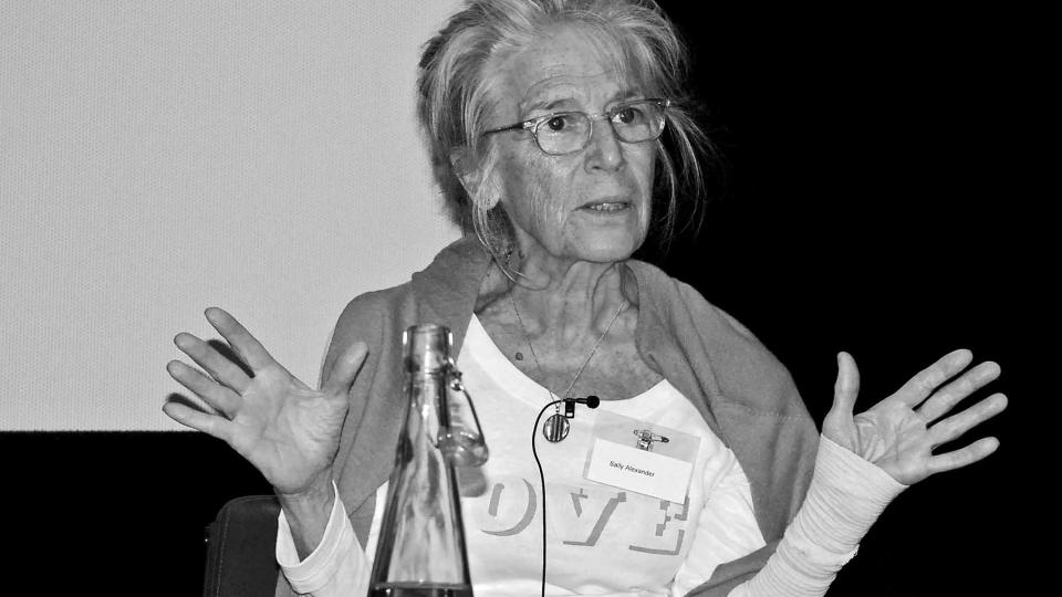 Sally Alexander is wearing glasses and a white shirt, the palms of her upright hands are showing.
