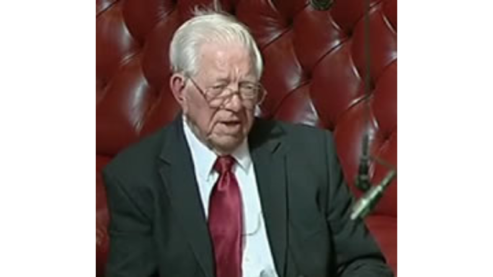 Jack Ashley is seated with glasses on, wearing a suit and tie.