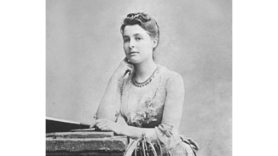 Beatrice Webb is posing sat with a dress on, stroking her chin with her hand.