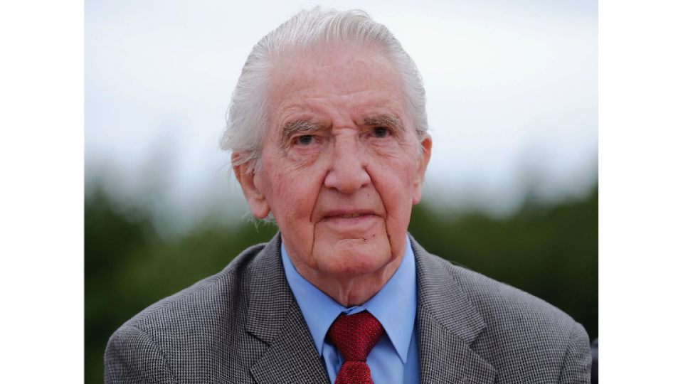 Dennis Skinner has grey hair and is wearing a smart grey suit and red tie.