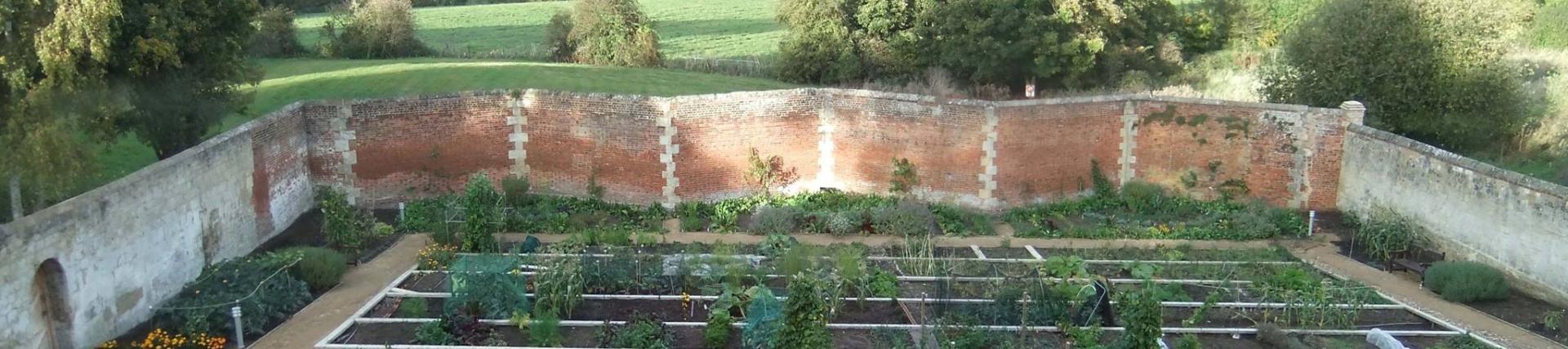 The full crinkle crankle shape of the walled garden. Inside the walls is vegetable beds and beyond the walls is green fields and trees.